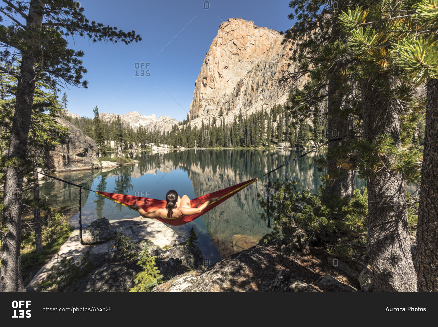 Female hiker relaxing in hammock between two pine trees overlooking Elephants Perch and Saddleback Lake, Sawtooth National Recreation Area, Stanley, Idaho, USA