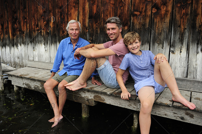 Boy sitting with grandfather and father together on jetty in summer