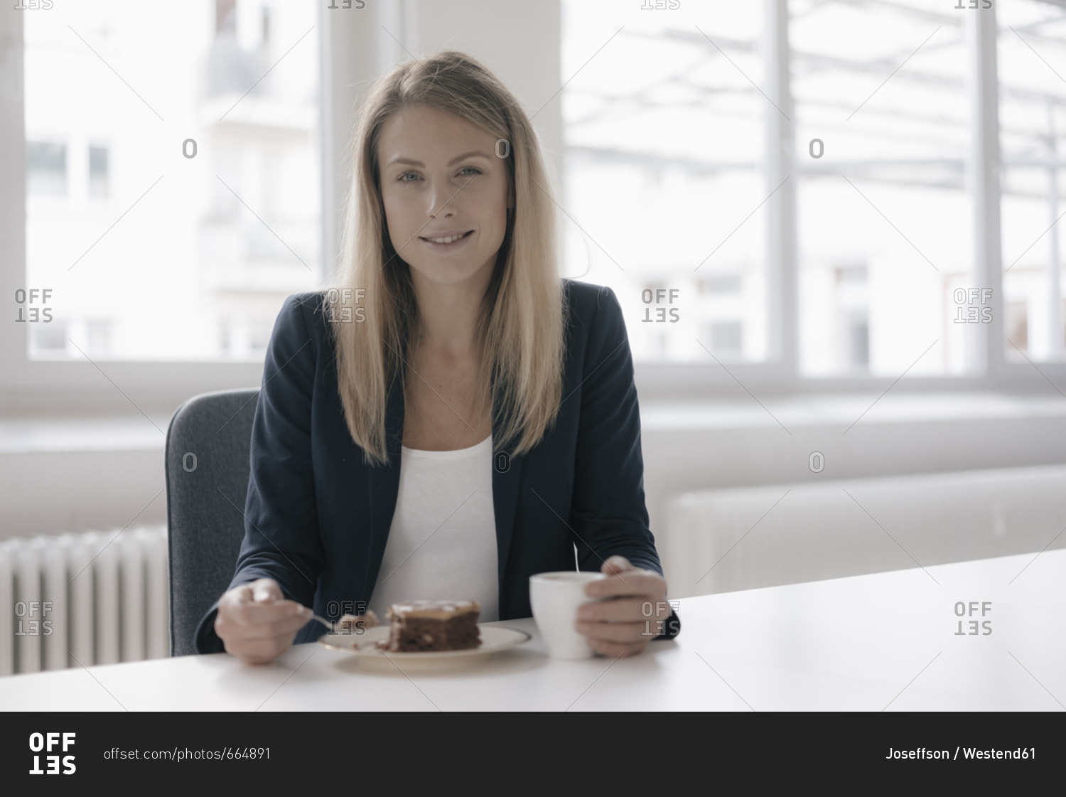 Portrait of smiling businesswoman having coffee and cake at desk in the office
