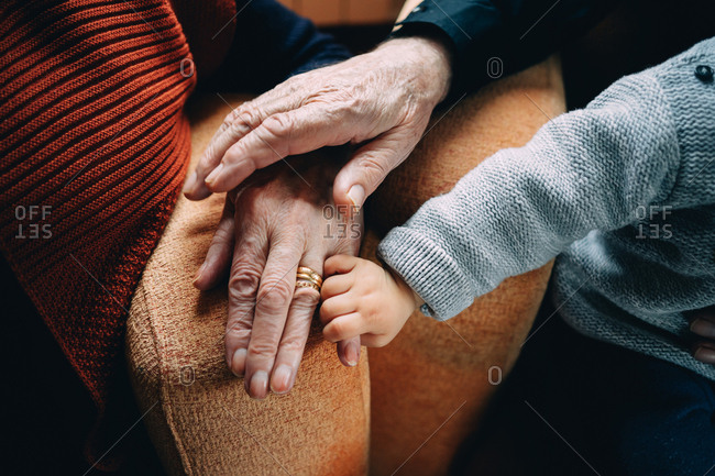 Toddler grasping grandparents resting hands on armchair