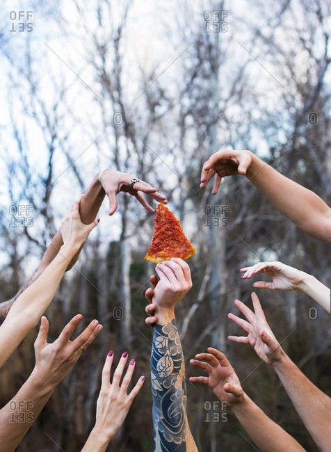 Crop shot of tattooed person holding pizza slice and hands trying to reach it in fight