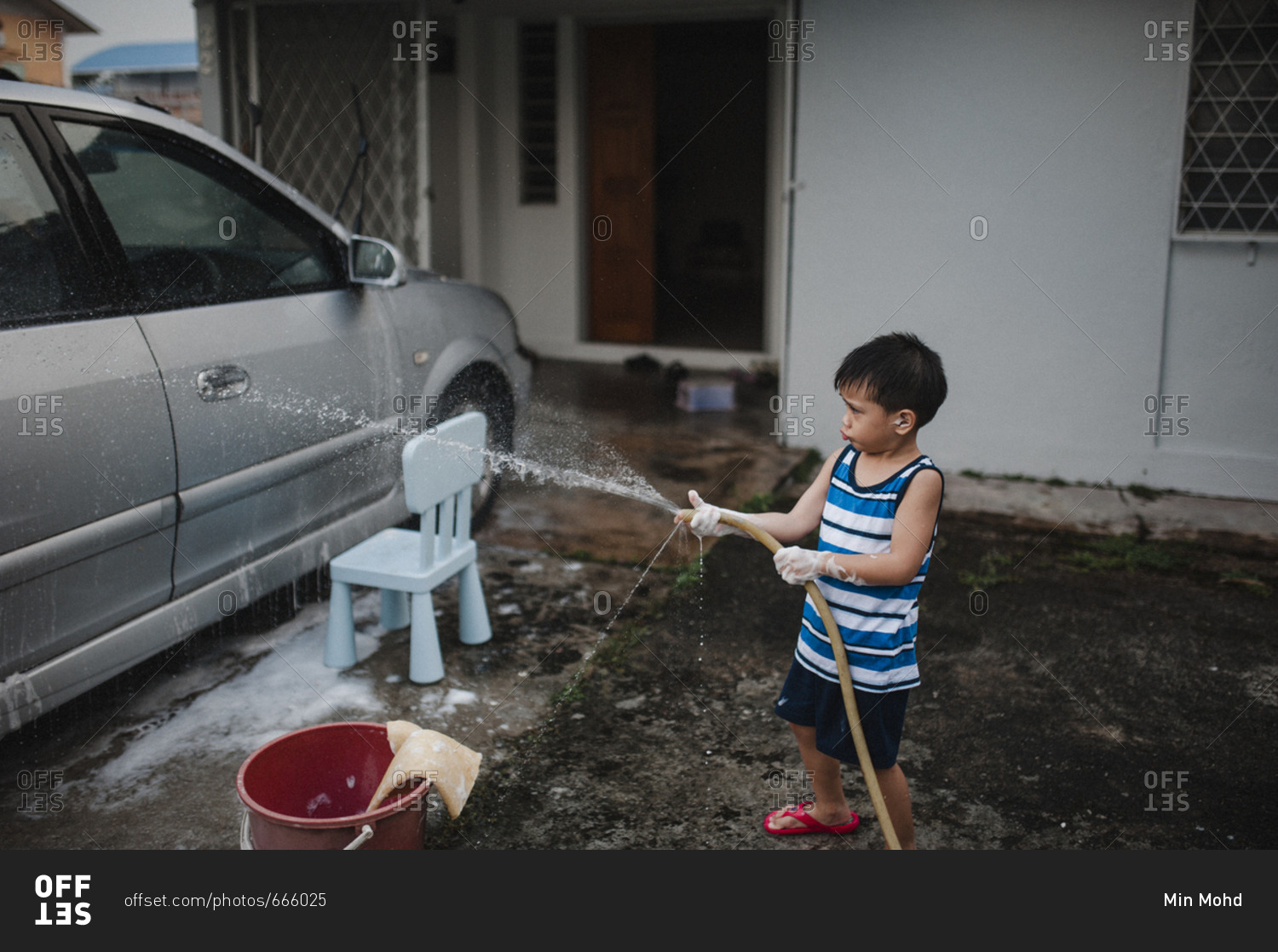 Little boy washing car with soap and a garden hose