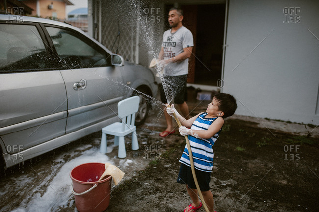 Little boy washing car with his dad and a garden hose