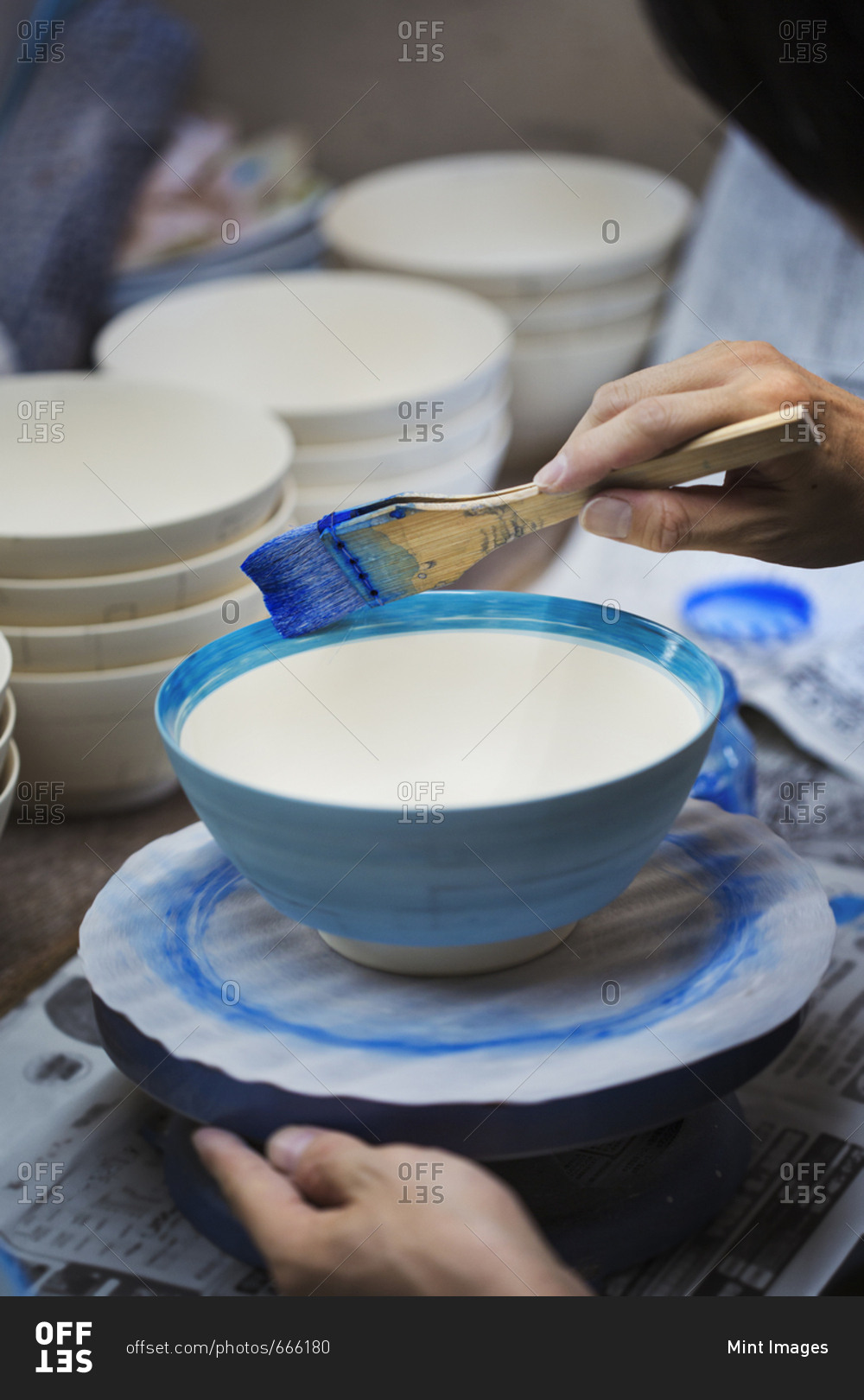 Close up of person working in a Japanese porcelain workshop, painting white bowls with blue glaze