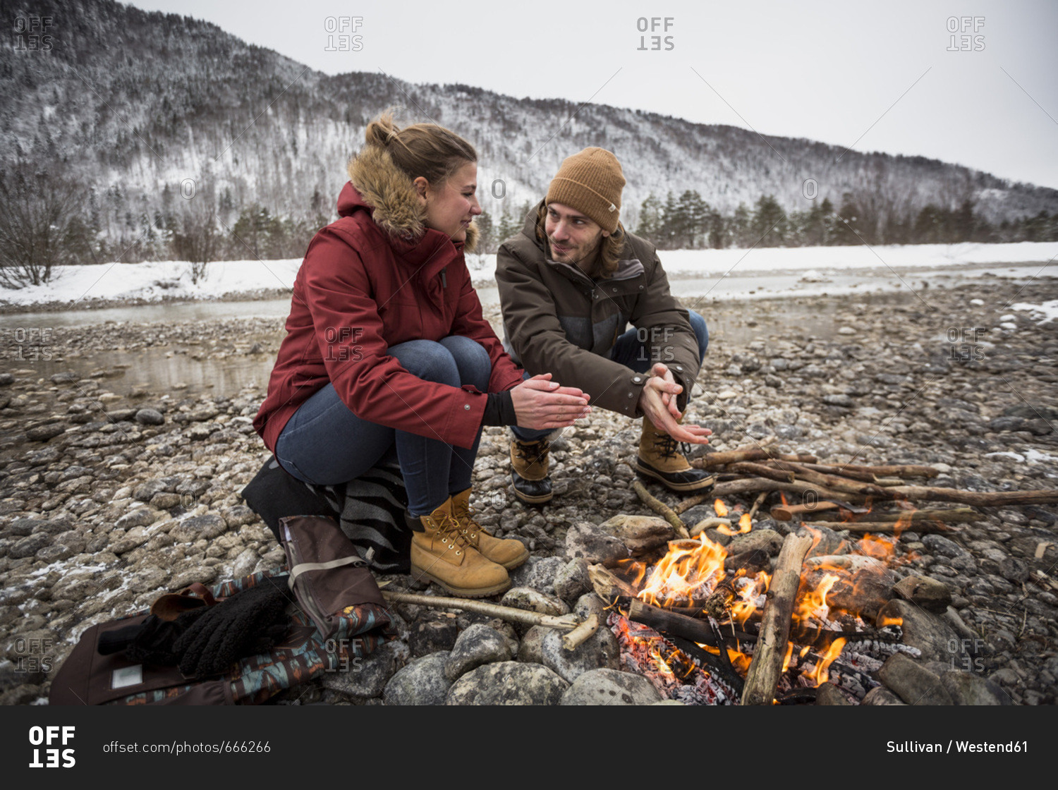 Couple on a trip in winter warming hands at camp fire