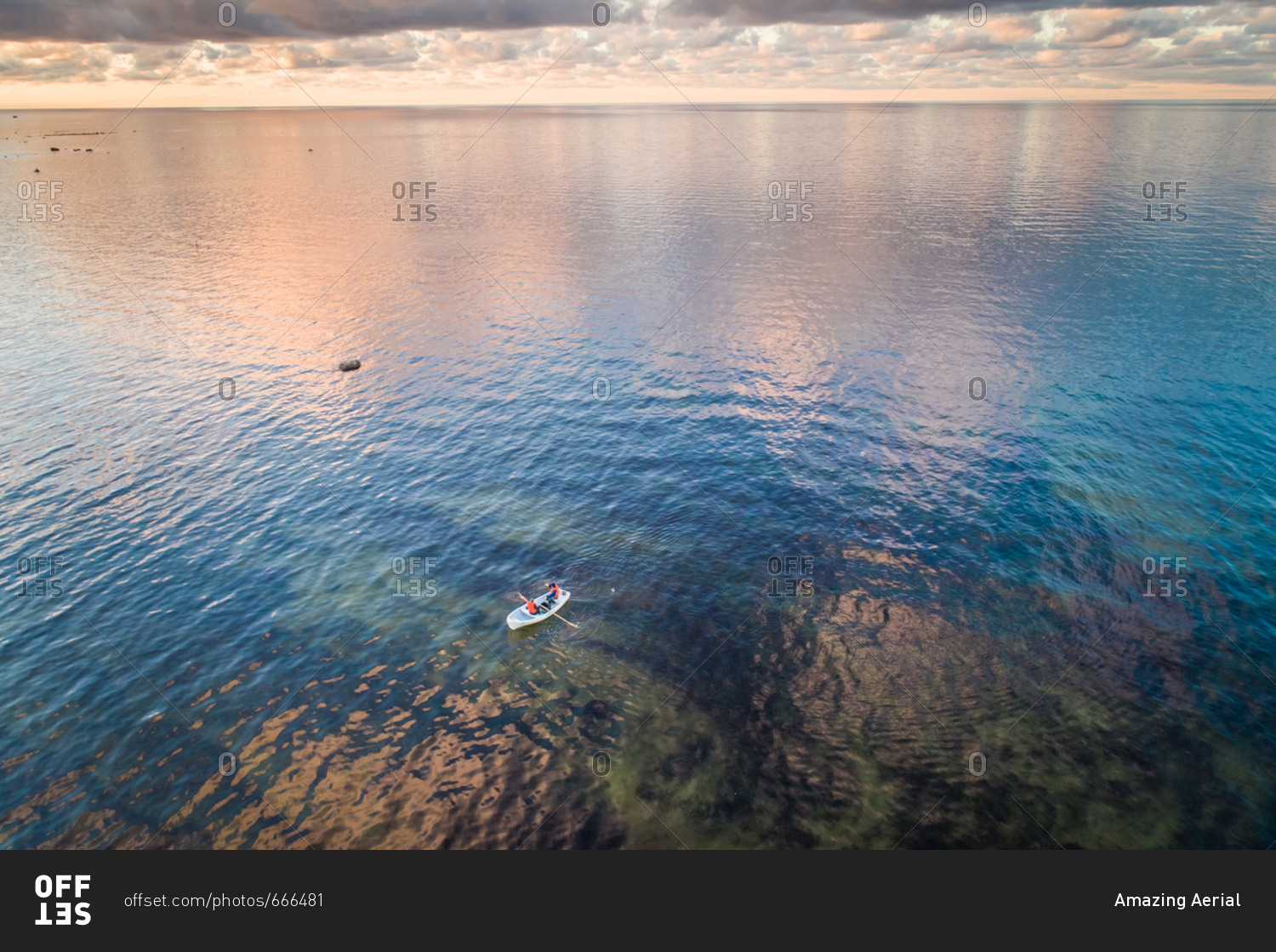 Aerial view of two people in a small wooden boat in the colorful baltic sea at sunset