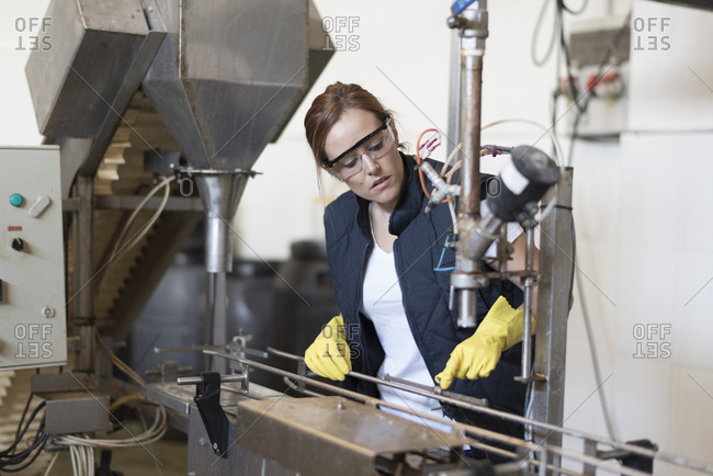 Worker woman revises machine in factory with protective glasses and gloves