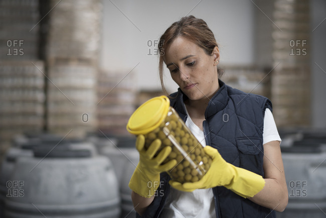 Woman looking olives bottle quality in food factory with barrels background