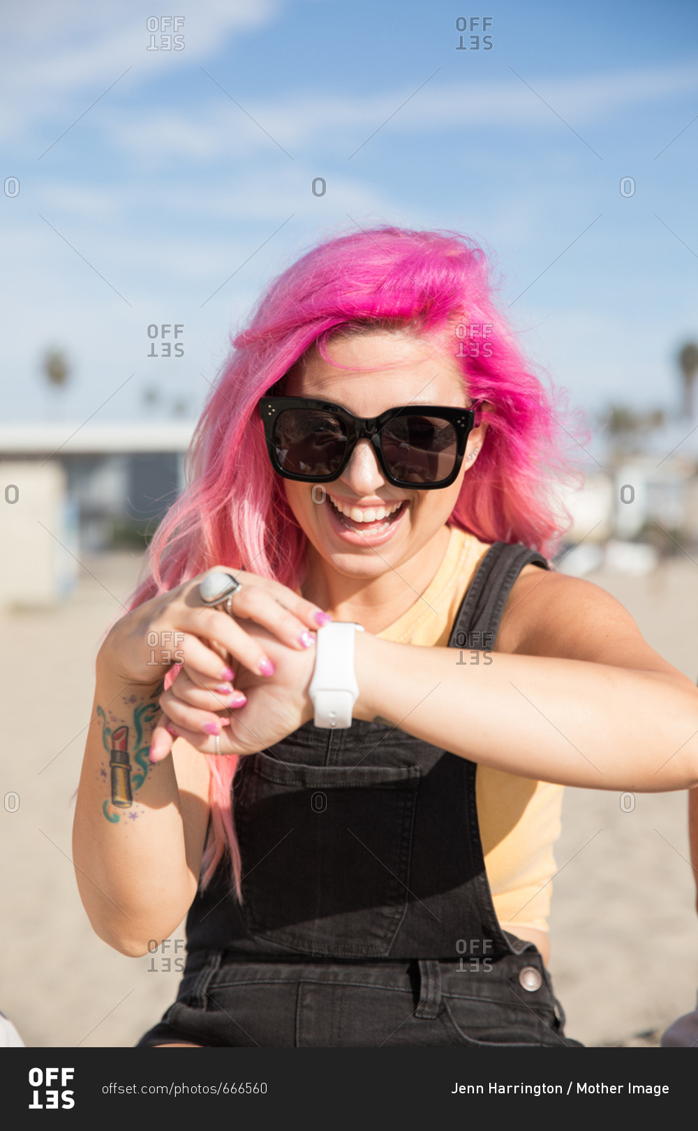 A woman looks at her watch, wearable tech, while sitting at the beach so she can connect to work and email