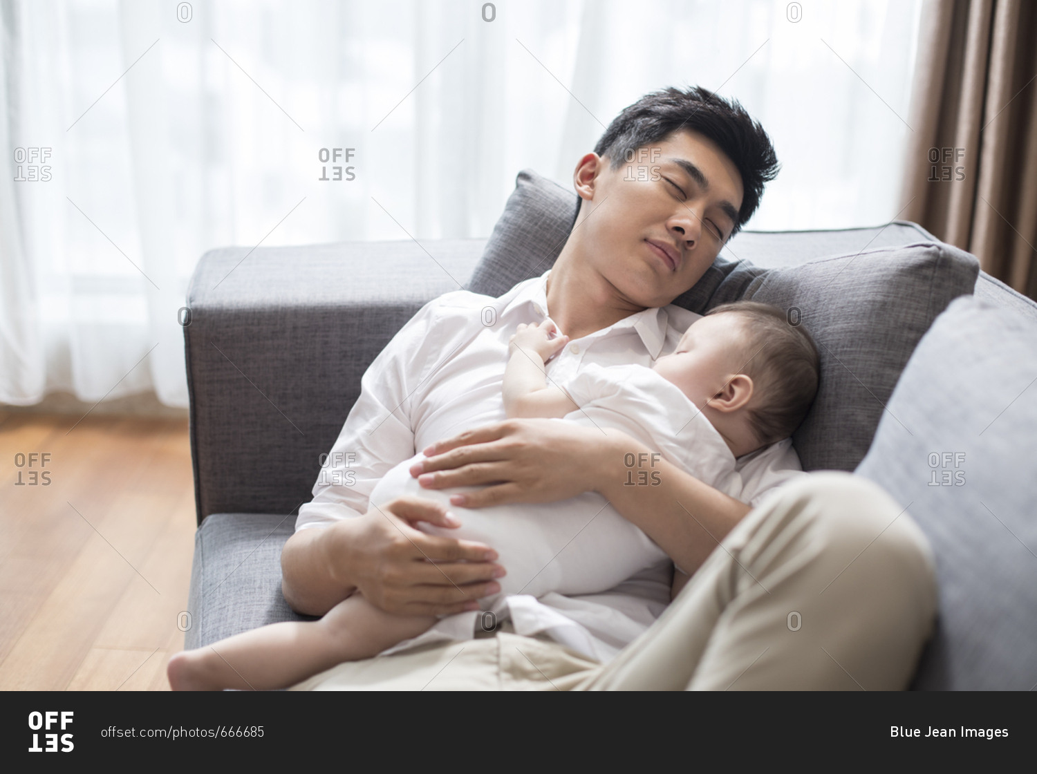 Young Chinese father and baby boy sleeping on sofa