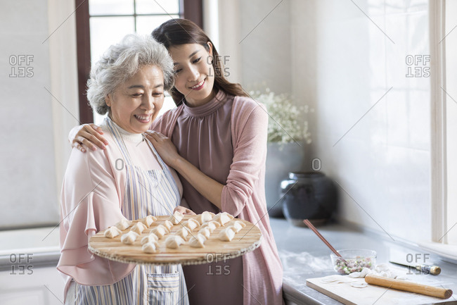 Cheerful Chinese mother and daughter making dumplings in kitchen
