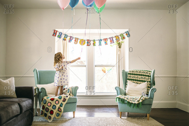 Girl decorating balloons in living room for birthday party stock ...