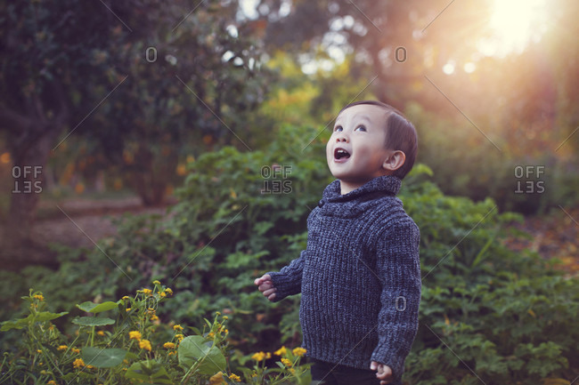 Cute playful baby boy with mouth open standing against plants at park