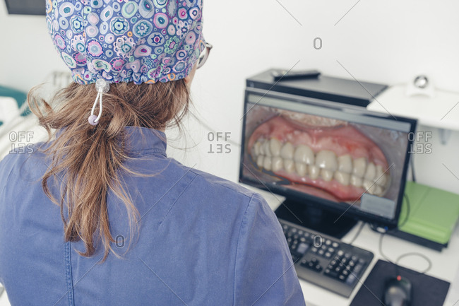 Rear view of female dentist looking at computer monitor in medical clinic