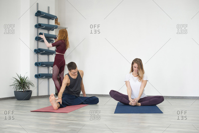 Yoga students stretching as another student puts away mat
