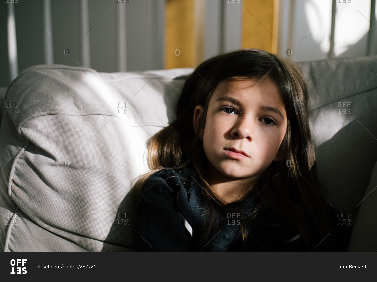 Little girl with dark brown hair sitting on sofa in sunlight stock photo -  OFFSET