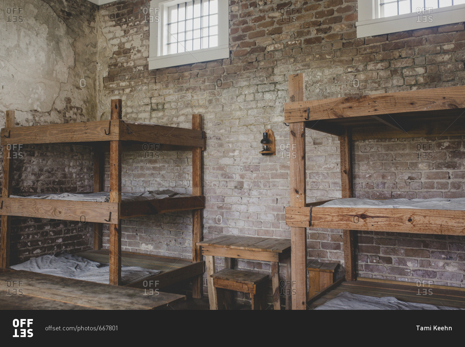 Empty jail cell with brick walls and wooden bunkbeds stock photo - OFFSET