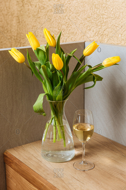 Yellow tulips in a vase beside a glass of wine
