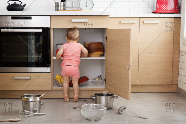 Rear View Of Baby Making Mess Of Kitchen Cabinets Stock Photo Offset