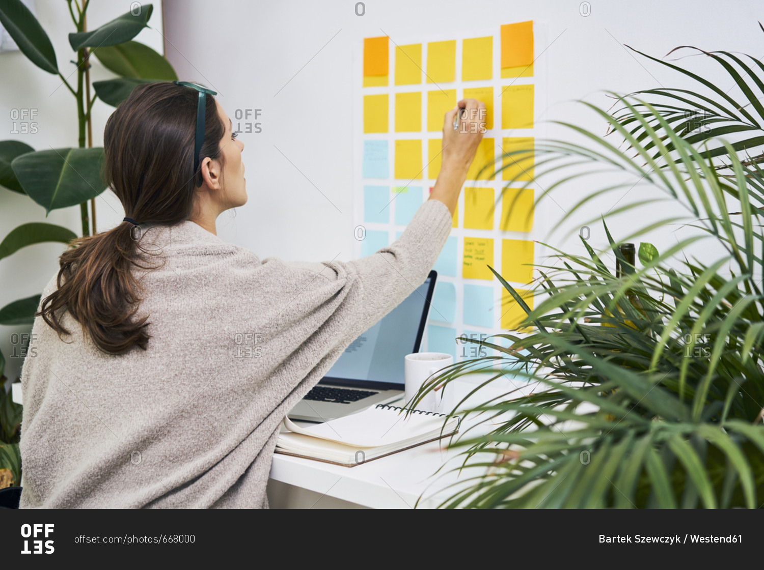 Young woman with laptop on desk working with adhesive notes on the wall