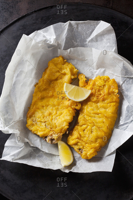 Fried coalfish filet and lemon slices on greaseproof paper