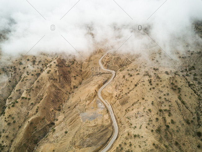 Aerial view of clouds falling on a serpentine empty road in the deserted landscapes of Ethiopia.