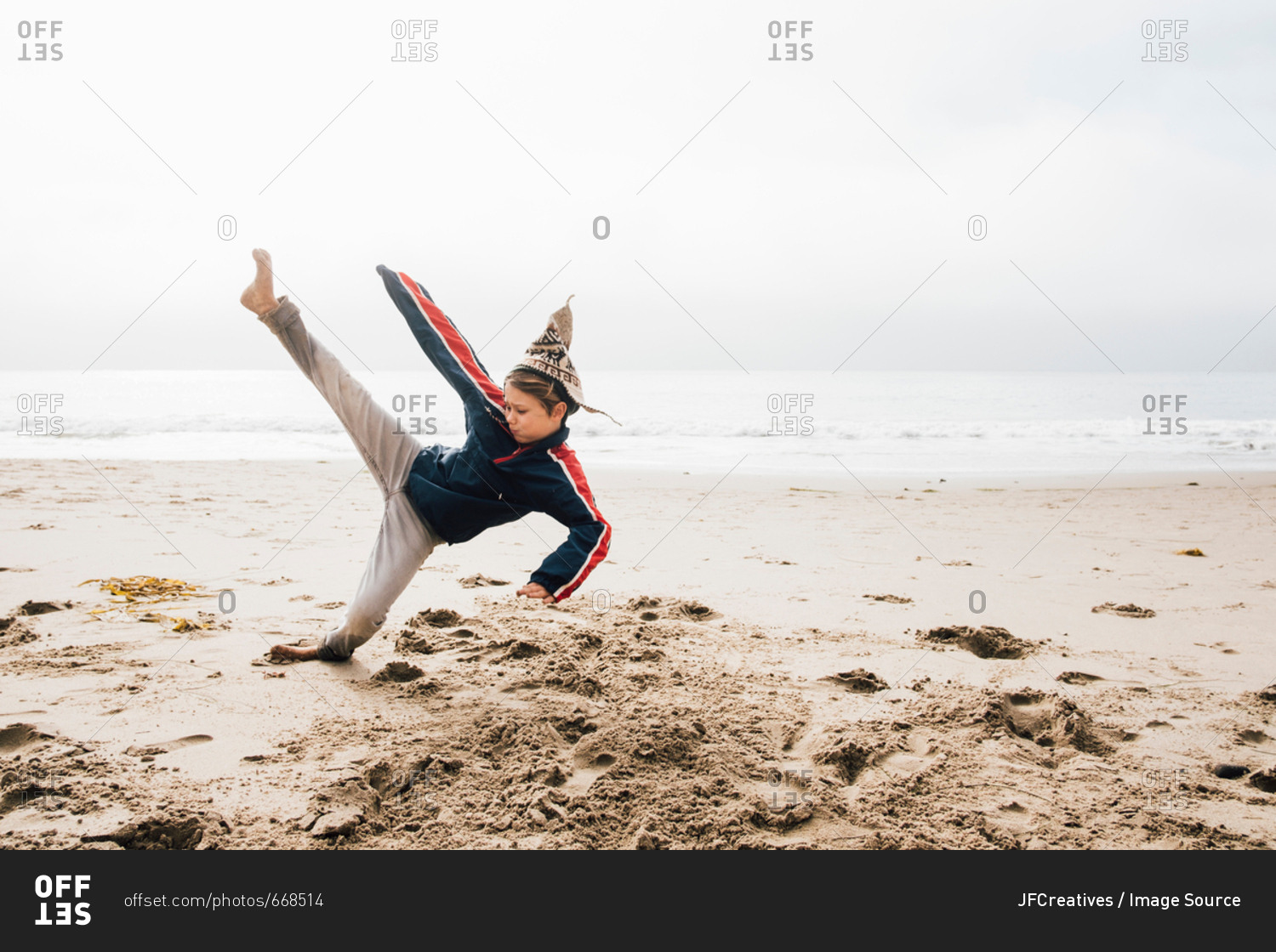 Young boy on beach, practicing martial arts, leg raised in kick