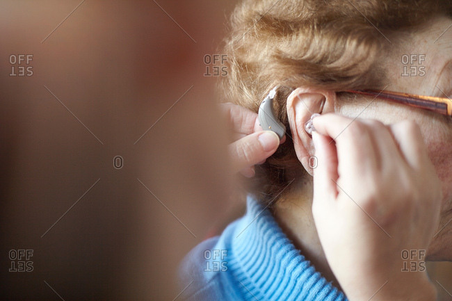 Mature woman helping senior woman insert hearing aid, close-up, differential focus