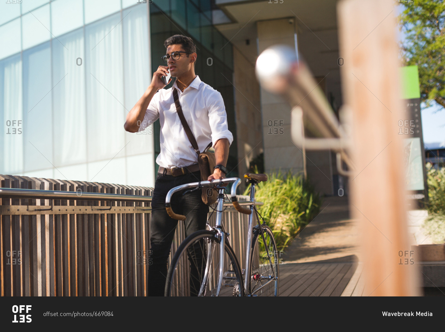 Businessman talking on mobile phone while walking with his bicycle at office premises