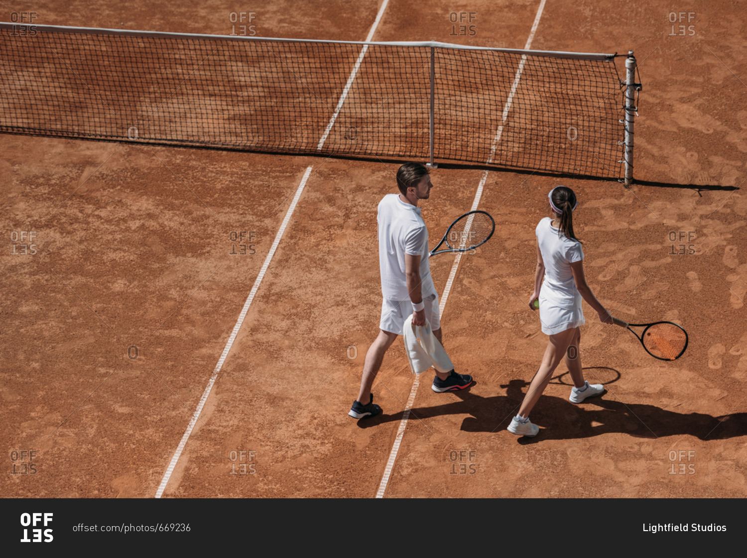 High angle view of young couple with rackets walking by tennis court