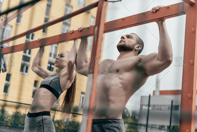 Side view of strong female in activewear doing pull ups on crossbar while  training on modern sports ground and looking away stock photo - OFFSET