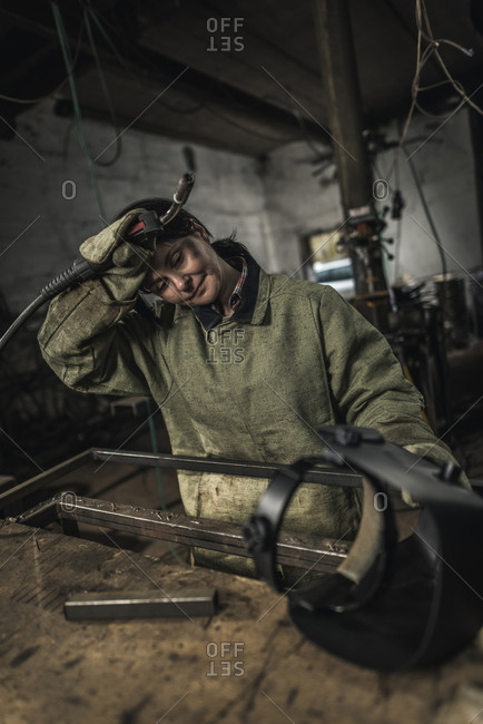 Tired female welder holding welding torch in workshop