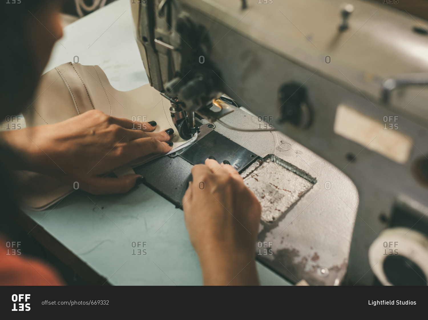 Close-up partial view of seamstress working with sewing machine and leather at shoemaker workshop