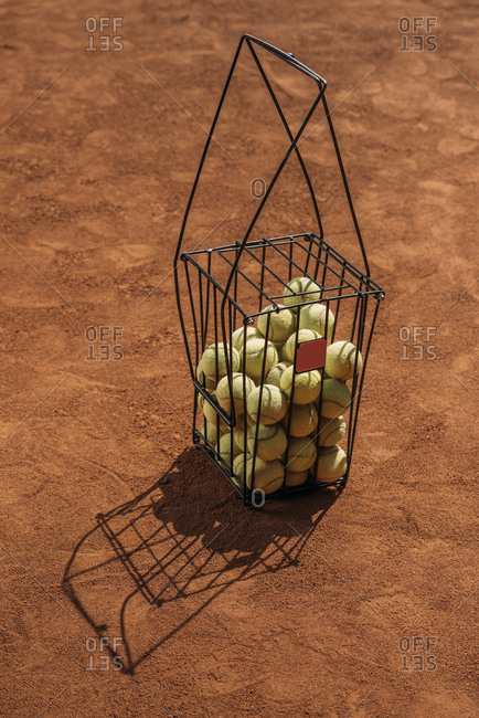 Basket of tennis balls standing on orange court surface