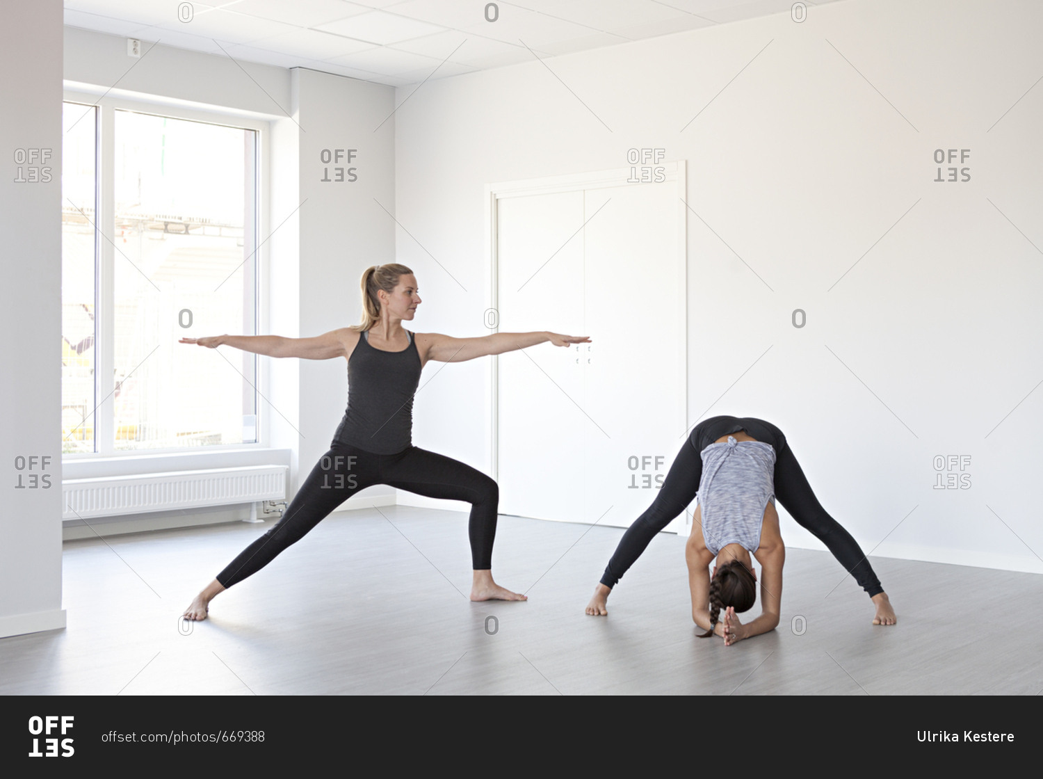 Young women in warrior two and wide legged forward bend poses during ...