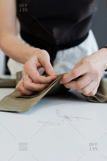 Close-up view of unrecognizable female tailor pinning together fabric pieces with needle before sewing a seam on machine