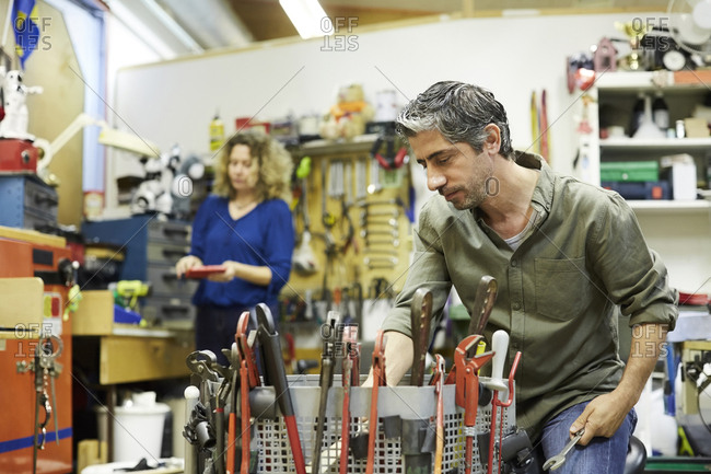 Mature male volunteer working with tools against female colleague at workshop