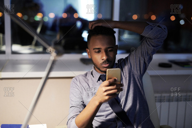 Young office manager sitting at table and checking Smartphone in the evening