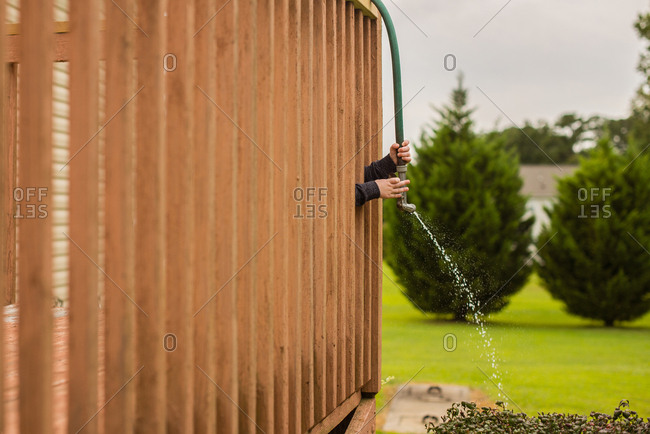 Child watering bush through deck railing