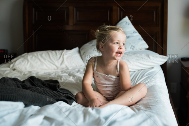 Little girl sitting cross legged on bed talking to no one in particular