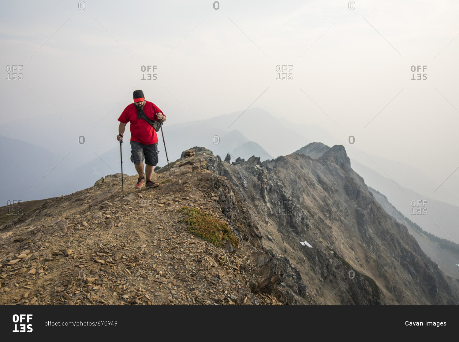 Full length of hiker using hiking poles while walking on mountain against sky