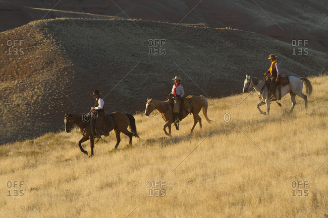 USA, Wyoming, Shell, The Hideout Ranch, Cowboys and Cowgirl Riding Horses in the Golden Light at End of Day