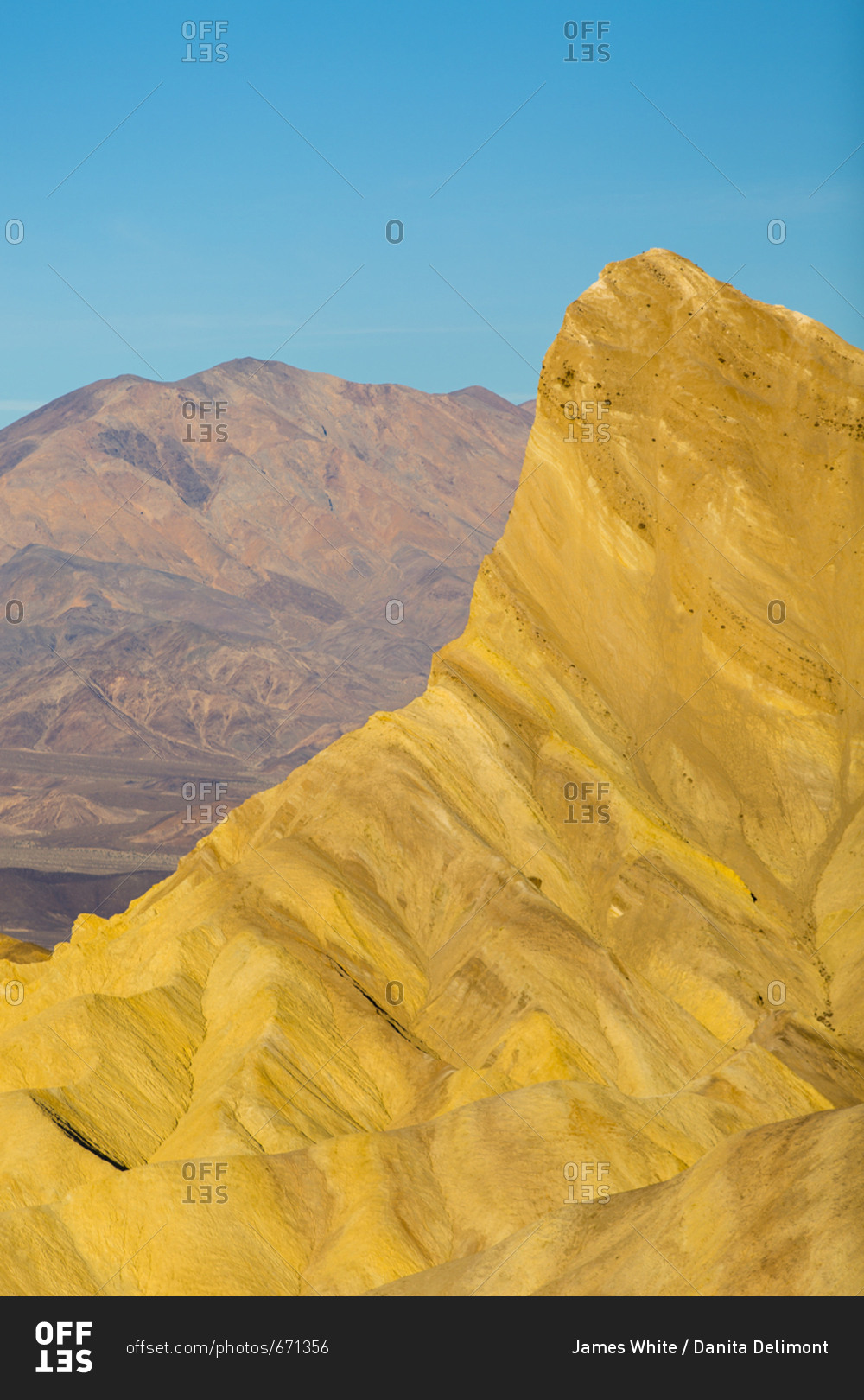 Warm light shines on Manly Beacon in the Golden Canyon in Death Valley National Park with a blue sky in the background