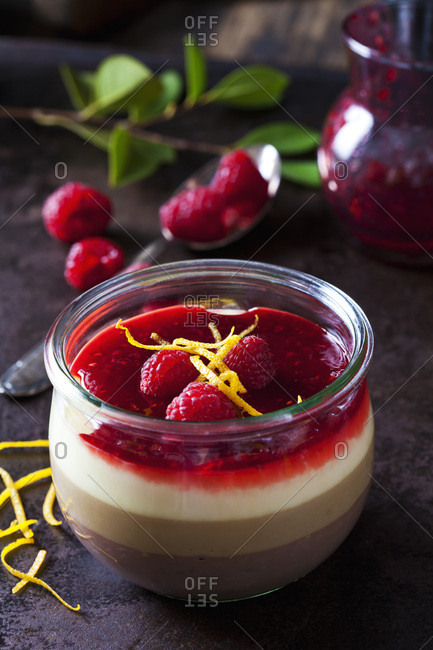 Glass of pudding with vanilla sauce and raspberry sauce garnished with raspberries and orange zest