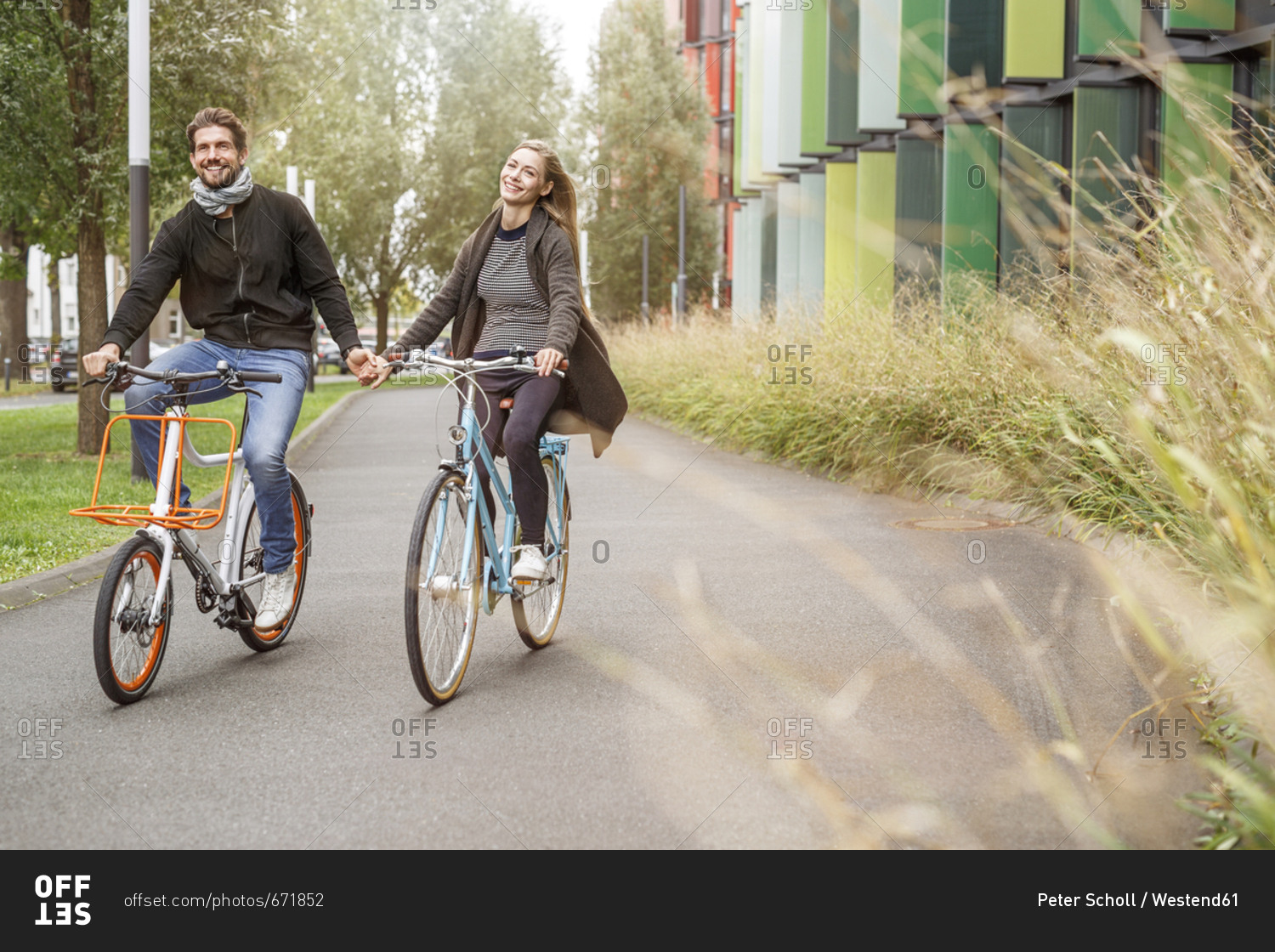 Happy couple riding bicycle hand in hand on a lane