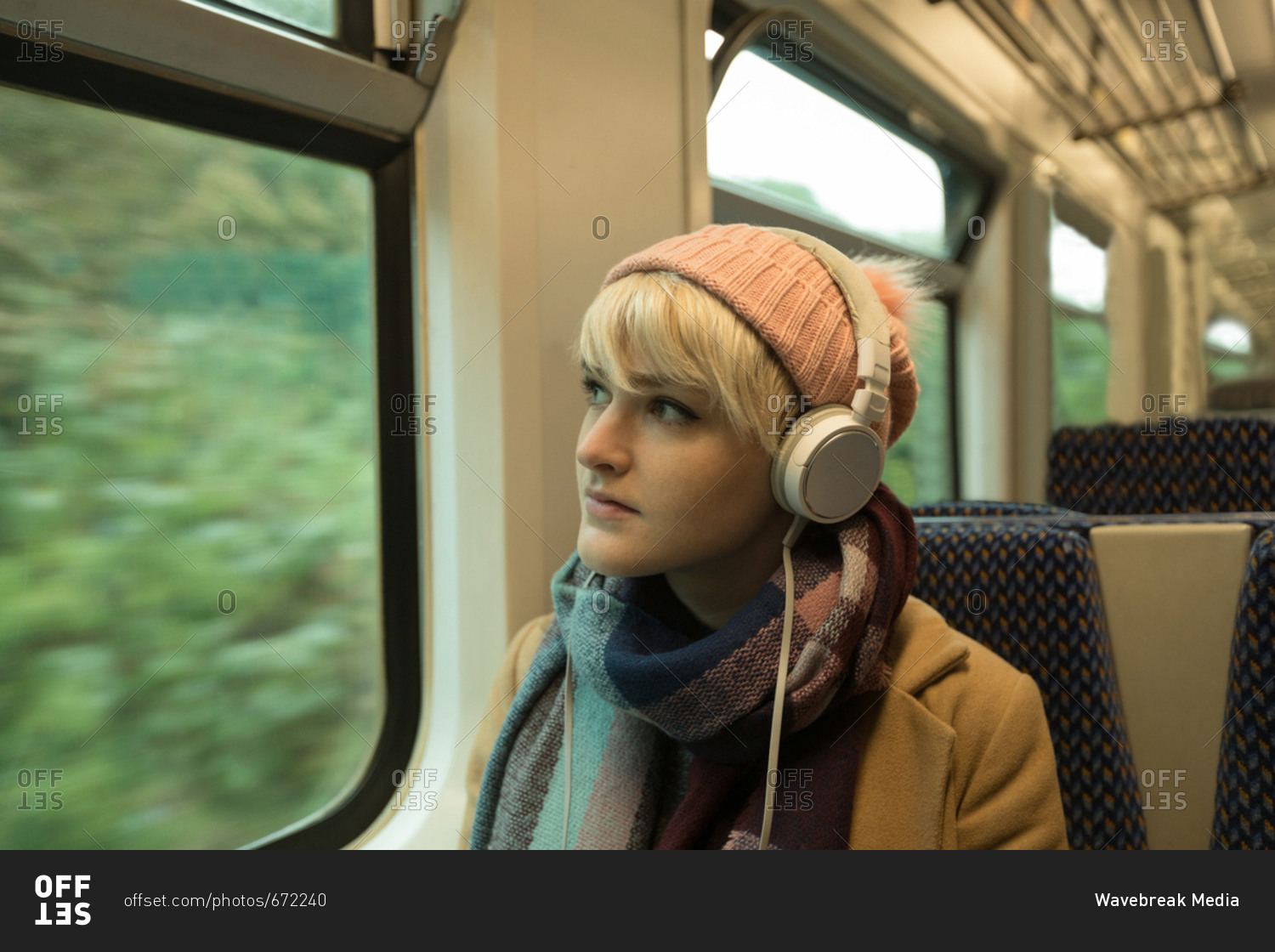Young woman in warm clothing listing to music on headphones