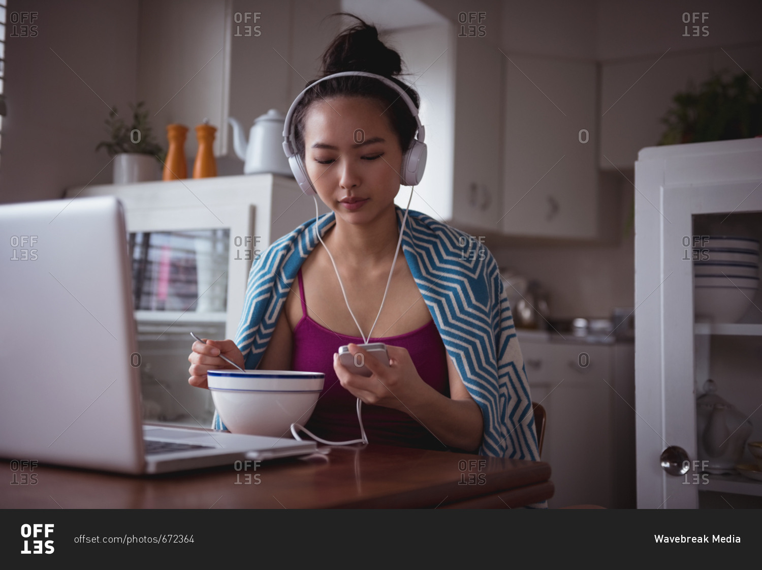 Woman listening music on mobile phone while having breakfast