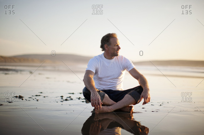 Mature man sitting cross-legged on the beach