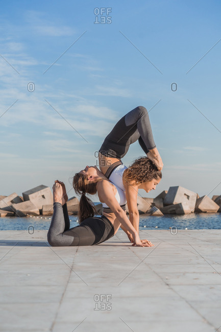 two young women on the beach in a paired acrobatic yoga pose Stock