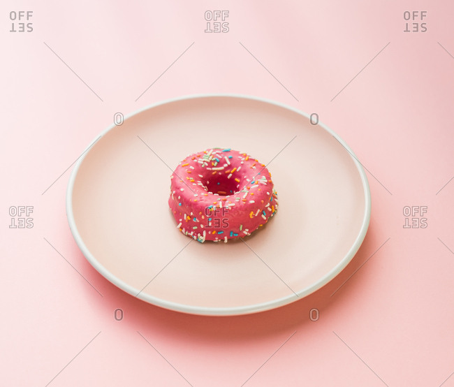 Minimalist arrangement of glazed dessert with sprinkles on white round plate.